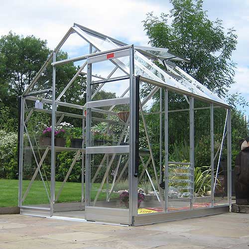 A free-standing 6x4 greenhouse with high eaves, featuring an aluminum frame, single fingertip sliding door, and placed on a solid ground surface.