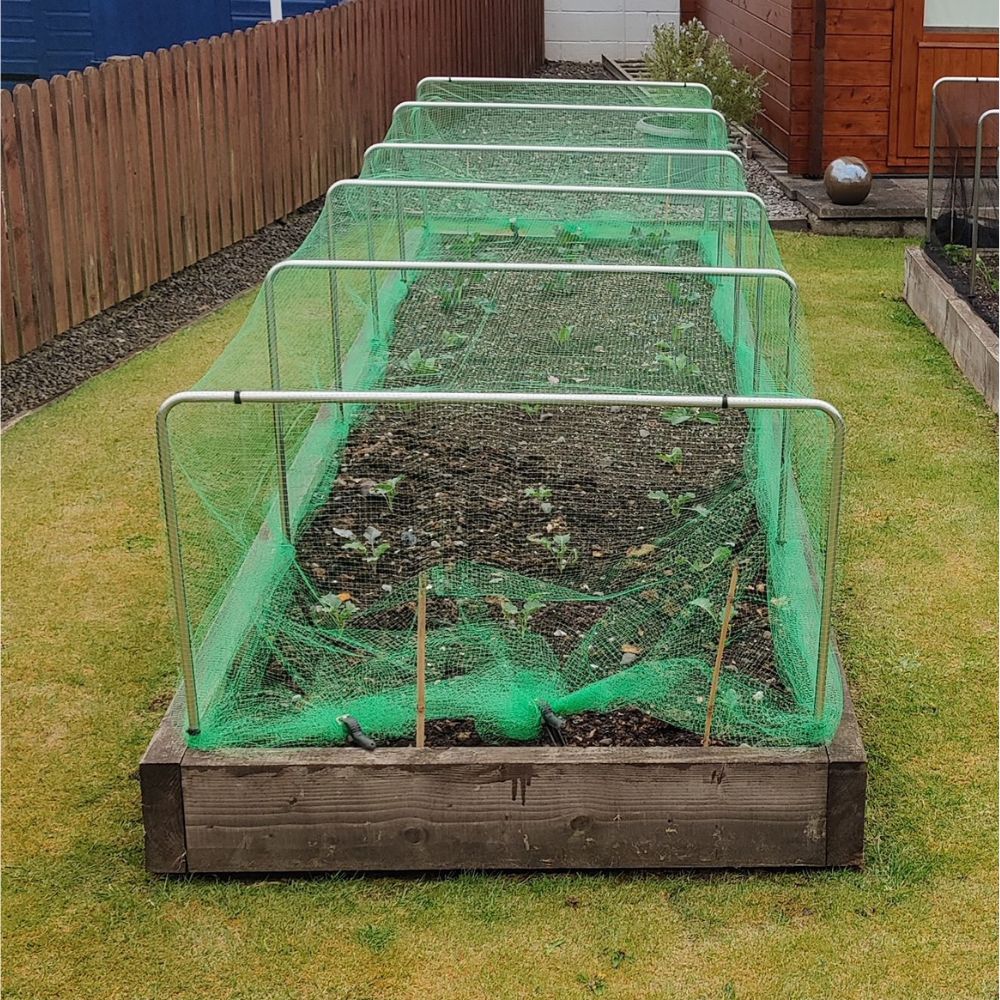 Row of raised garden beds with green netting on a grassy area.