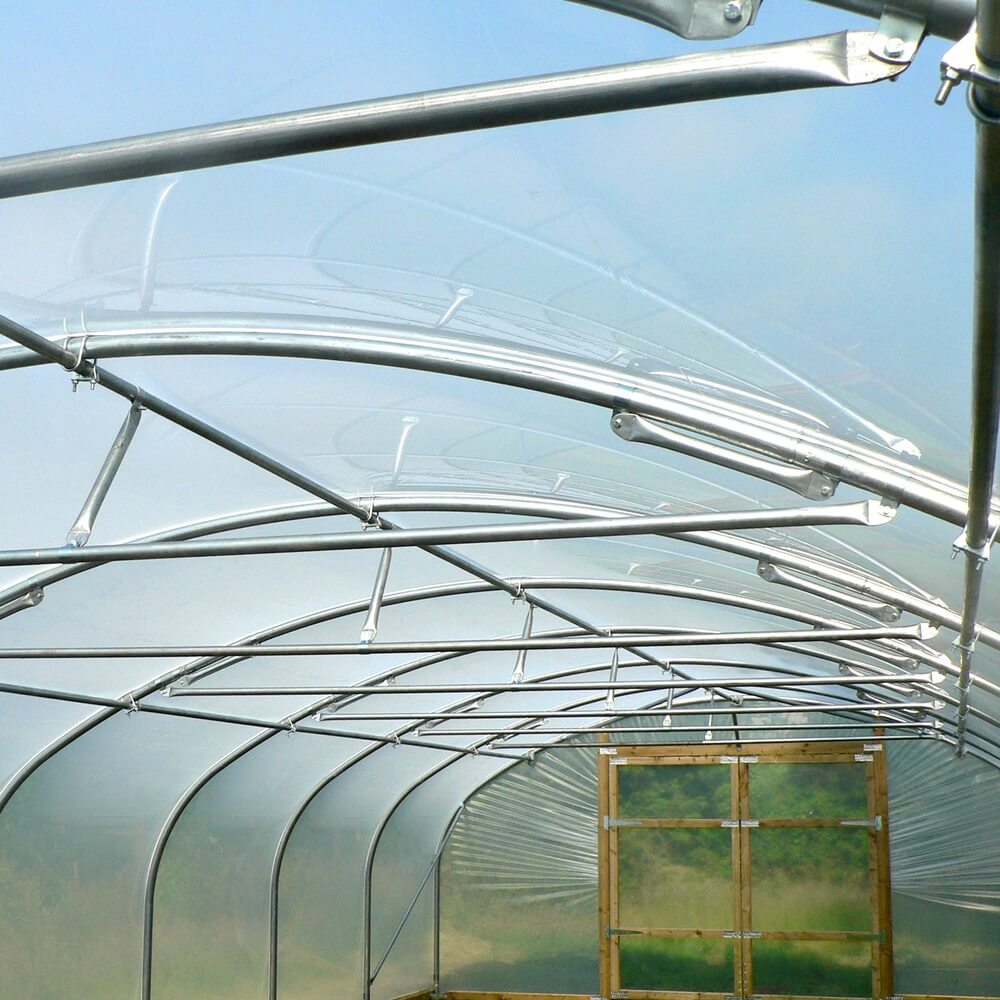 Greenhouse structure with curved roof and metal frame against a clear blue sky.