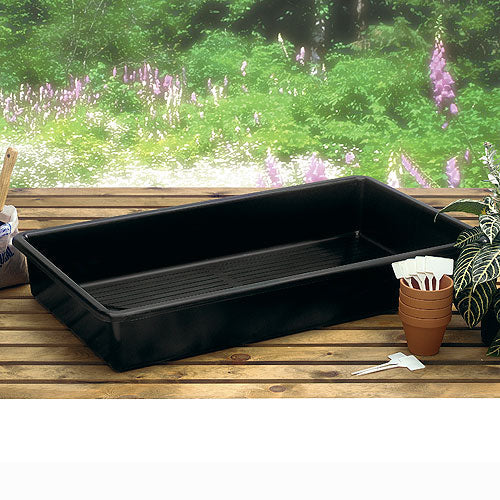 A black plastic watertight tray placed on a wooden surface, with a potted plant and some gardening tools