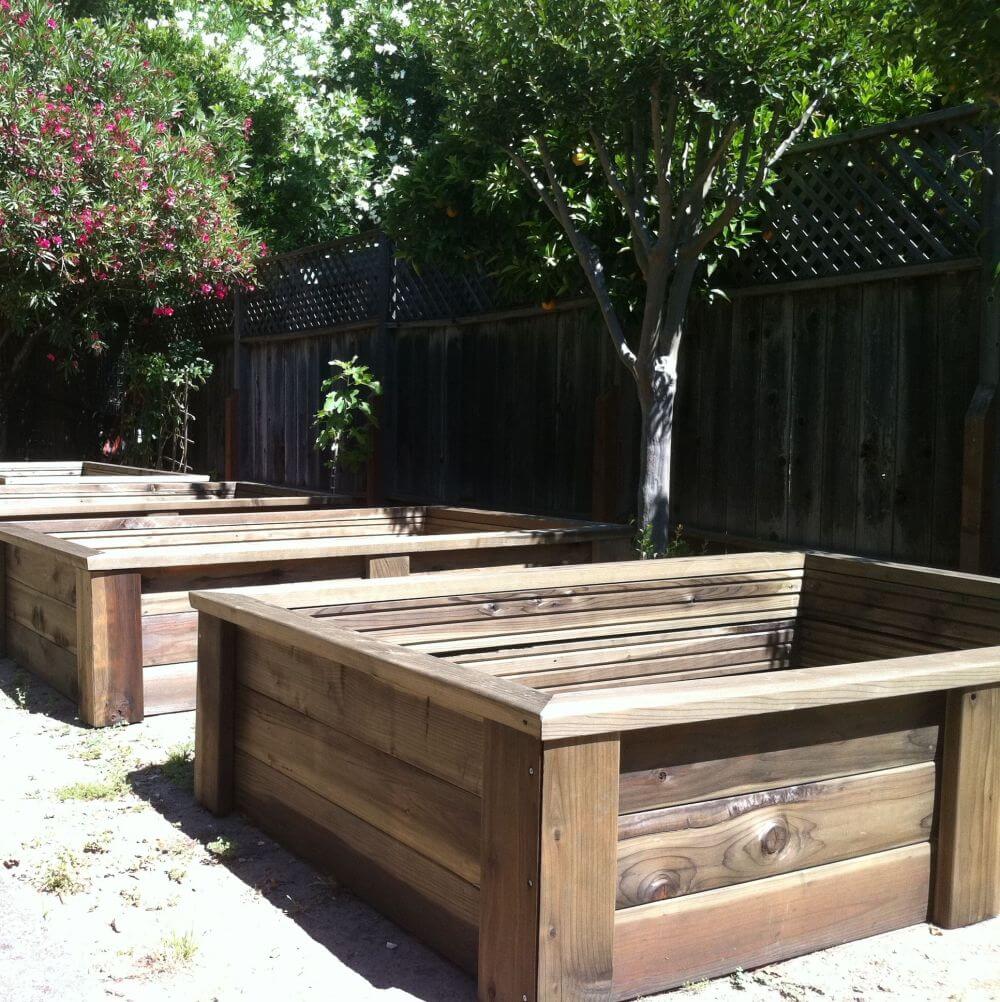 Wooden raised garden beds in a backyard setting with trees and plants.