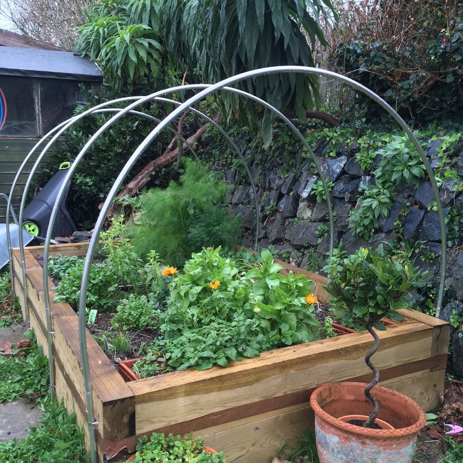 Wooden raised garden bed with garden tunnel stone wall in the background.