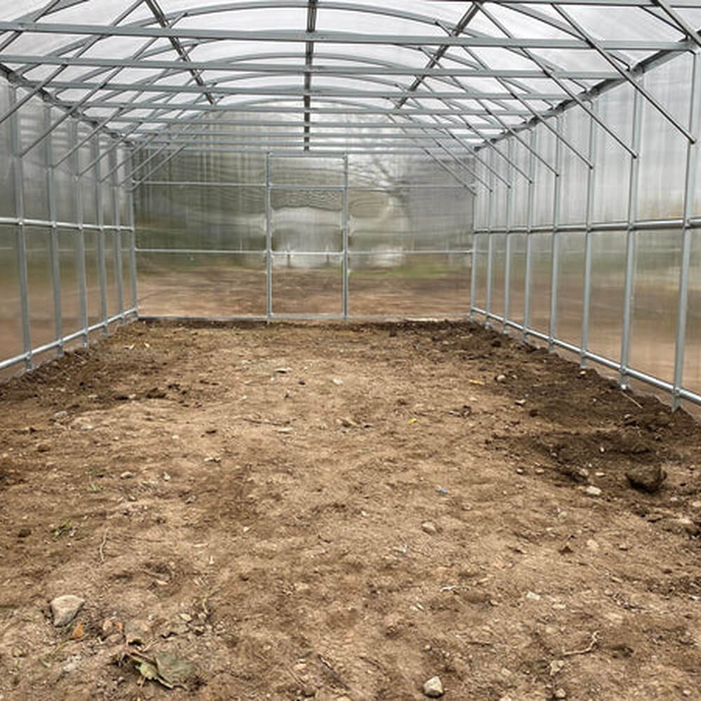 Empty greenhouse with soil floor and metal frame