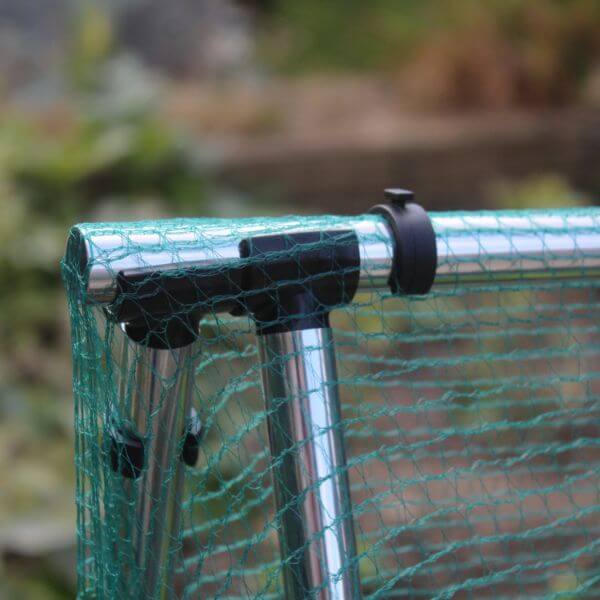 Close-up of a green mesh screen with metal frame and black clips against a blurred natural background