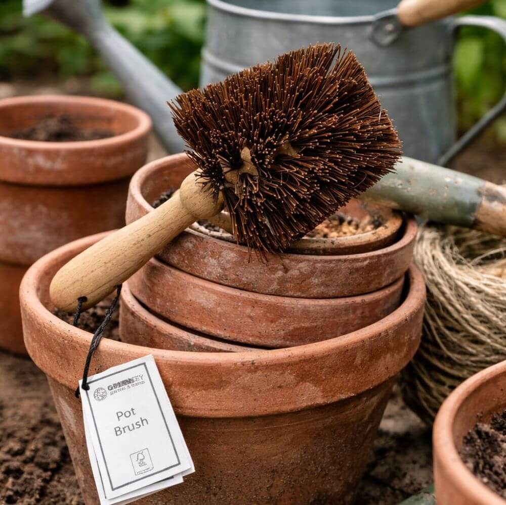 Pot brush on a stack of terracotta pots with a tag labeled 'Pot Brush' in an outdoor setting.
