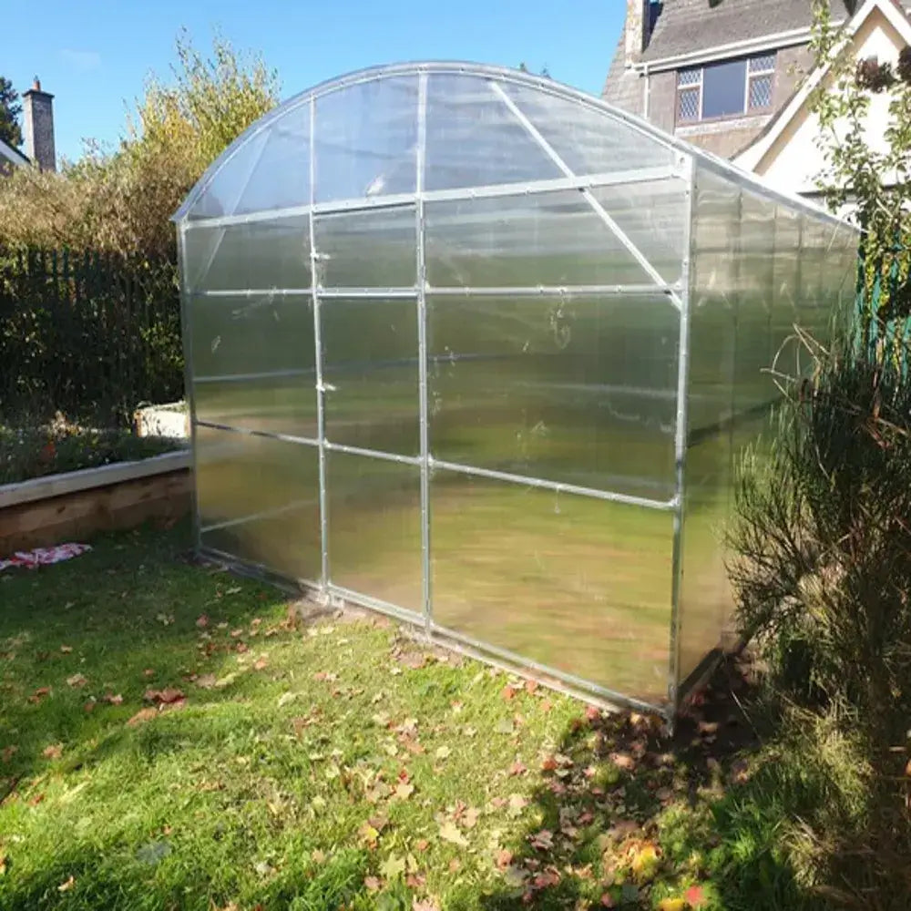 Clear polycarbonate greenhouse in a garden setting with a house in the background