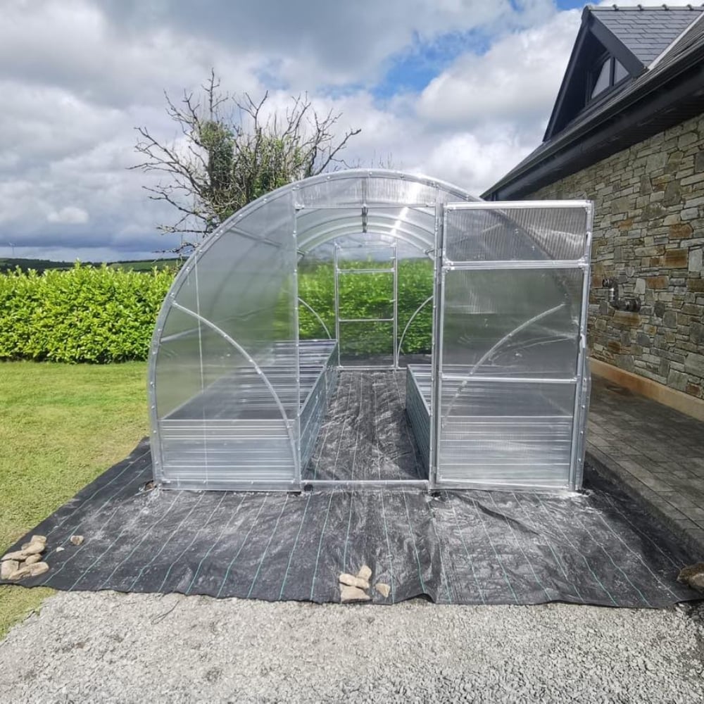 A polytunnel greenhouse with a metallic frame and clear polycarbonate covering