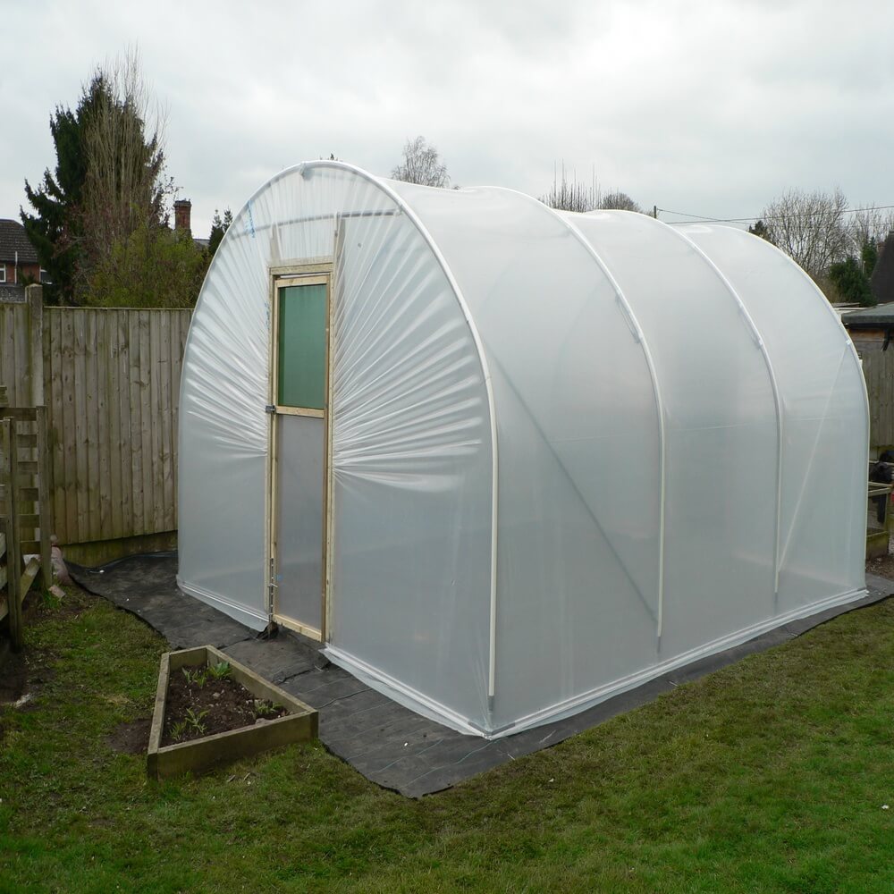 Polycarbonate greenhouse with a wooden door on a grassy area