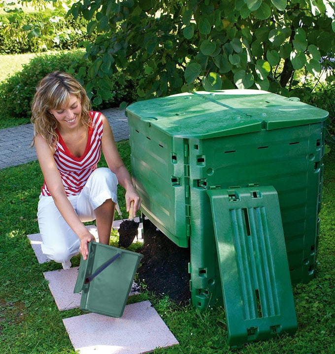 A person standing next to a green Thermo-King composting bin with a lid, in a garden setting. The bin is open, and there are gardening gloves on the person's hands.