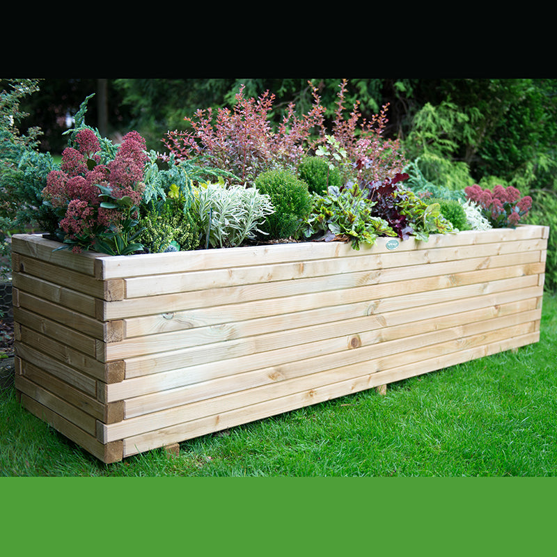 A wooden planter box filled with a variety of plants, placed on a grassy area.