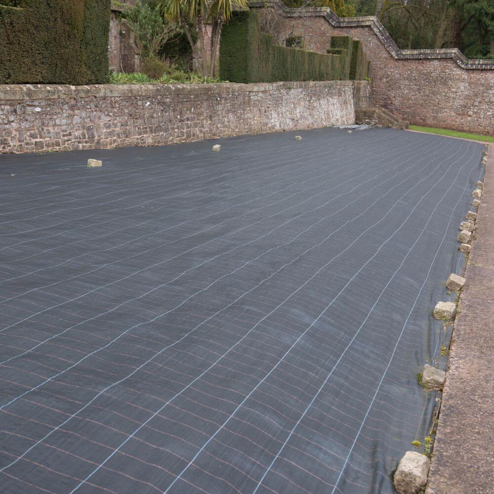 heavy duty landscape fabric laid out in garden by tone wall