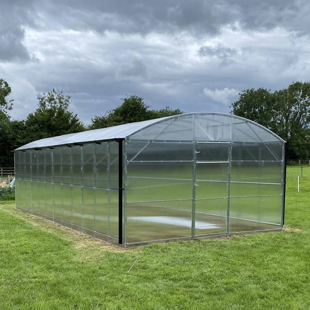 Large transparent greenhouse on a grassy field with trees in the background