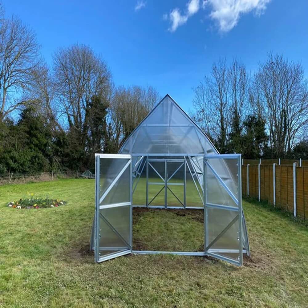 Greenhouse structure on a grassy area with trees and blue sky in the background