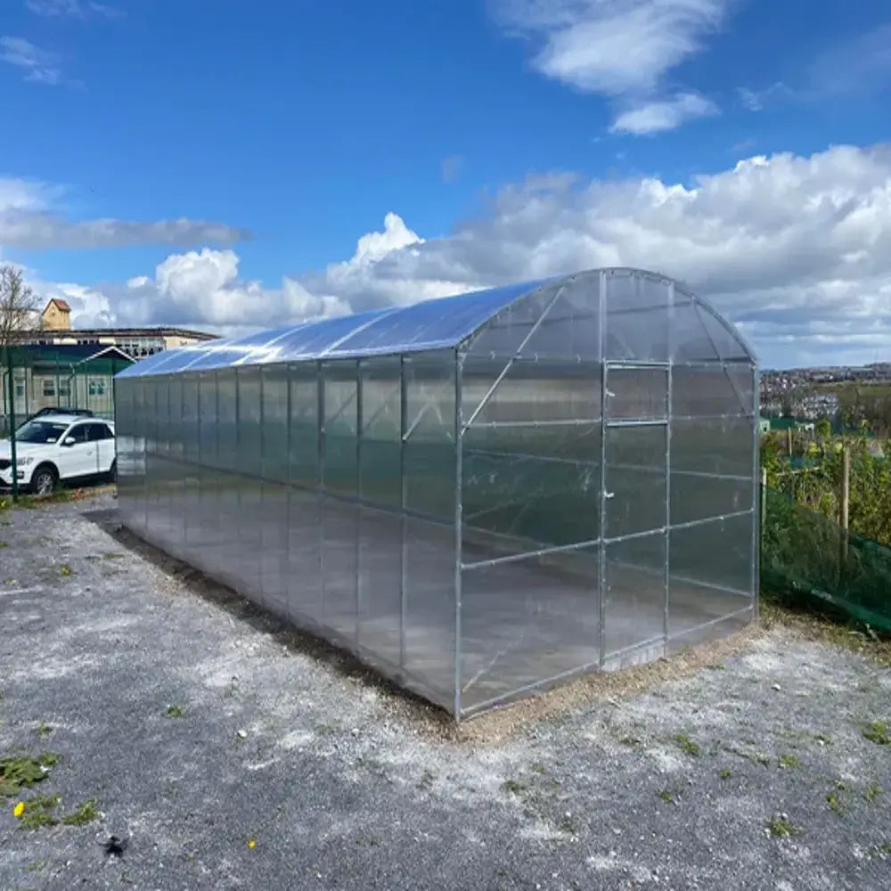 Large transparent greenhouse with a car parked nearby under a blue sky with clouds.