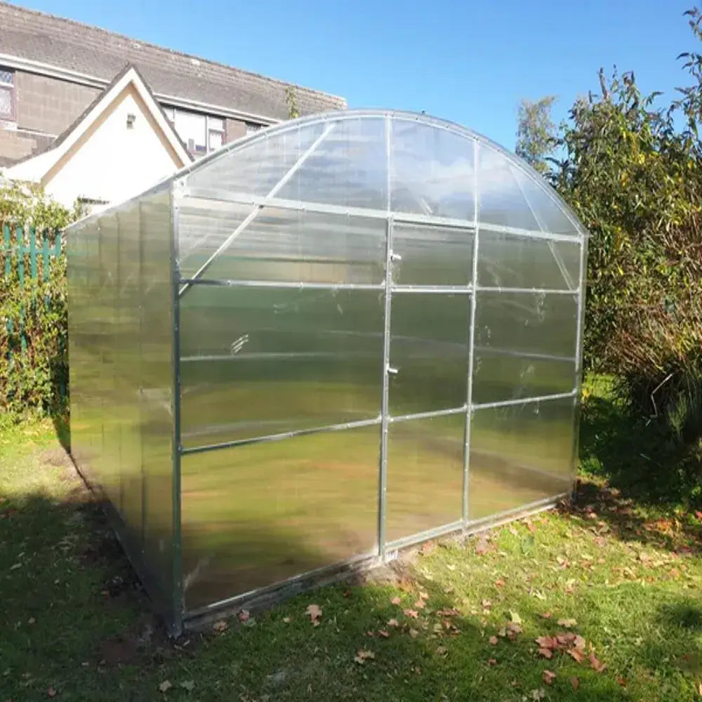 Clear polycarbonate greenhouse on a grassy area with a house and trees in the background