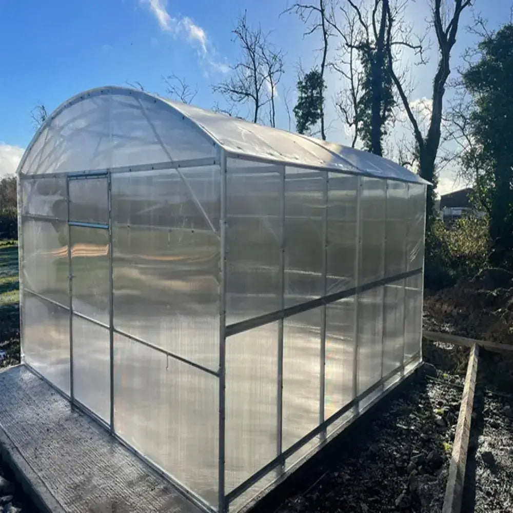 Clear polycarbonate greenhouse on a stand with trees and blue sky in the background