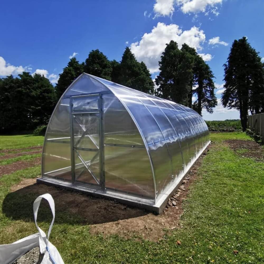 Greenhouse in a field with trees and blue sky