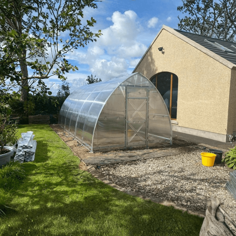 Polycarbonate greenhouse in a garden setting with a building in the background