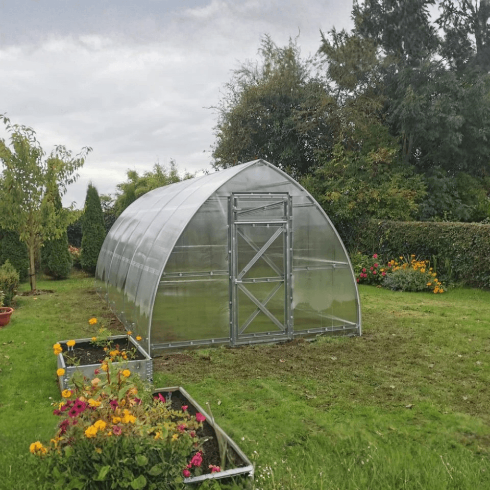 Polycarbonate greenhouse in a garden with flowers and plants around