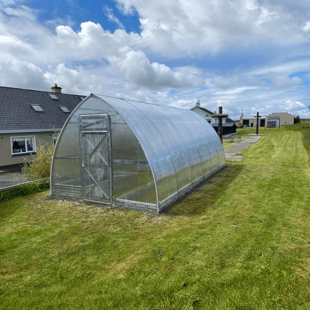 Greenhouse on a grassy area with houses and cloudy sky in the background