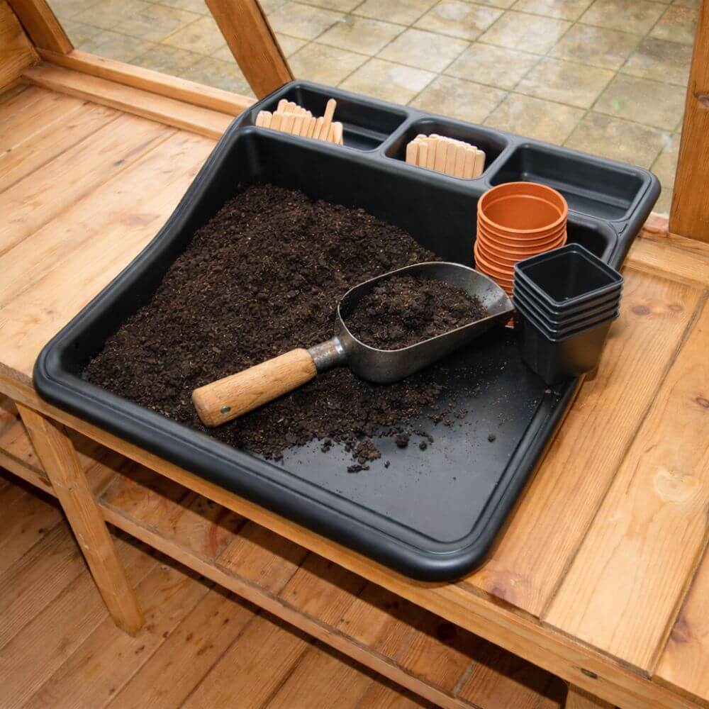 Gardening tray with soil, a scoop, and small pots on a wooden surface.