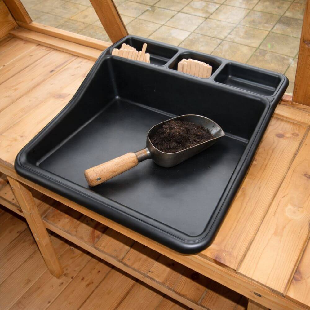Black tray with a scoop of soil on a wooden surface
