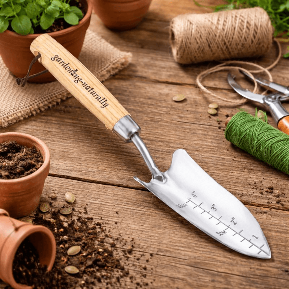 Gardening trowel with wooden handle on a wooden surface with gardening tools and plants.